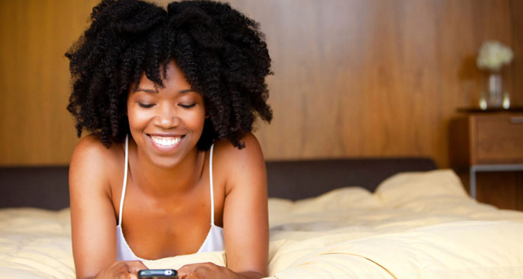 A black woman lying in bed using a cell phone.